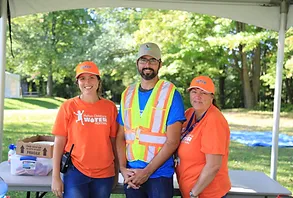 two female volunteers wearing orange halton children's water festival t-shirt stand beside a male volunteer wearing a safety vest, all three are smiling