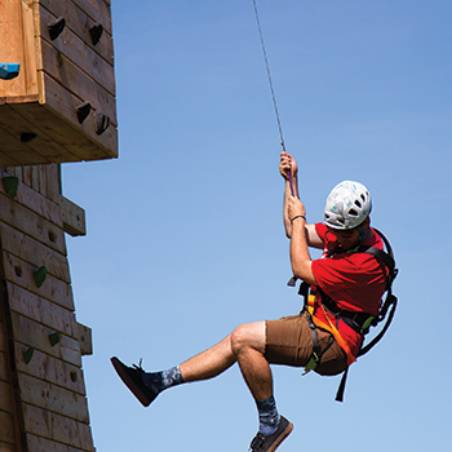 A young man in red repels down a rock-climbing wall