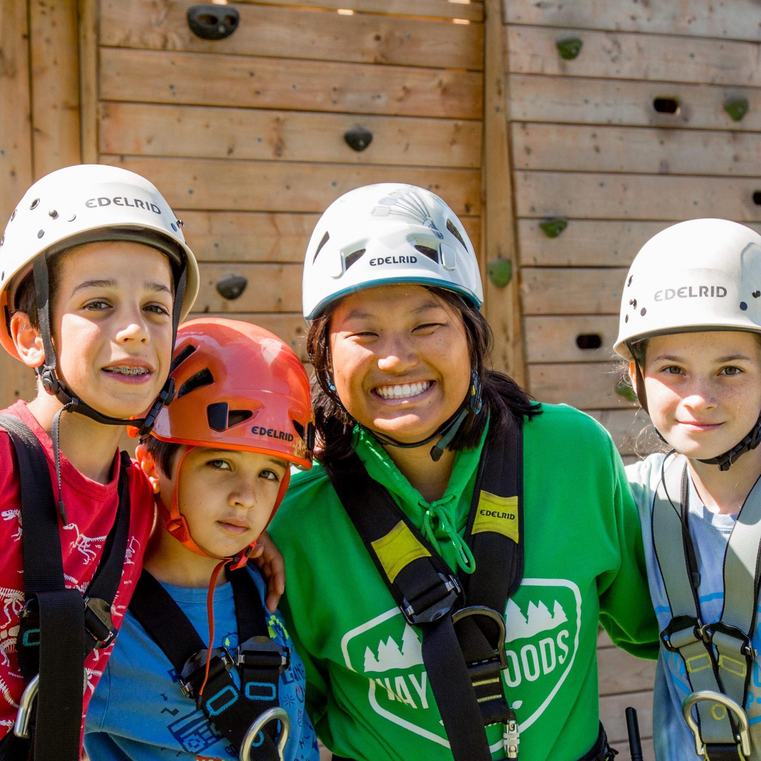 four kids smile for the camera while wearing rock climbing harnesses and helmets