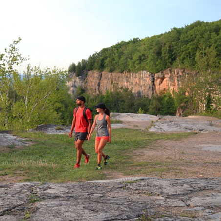 A man and a woman walk along a trail with the kelso cliff in the background