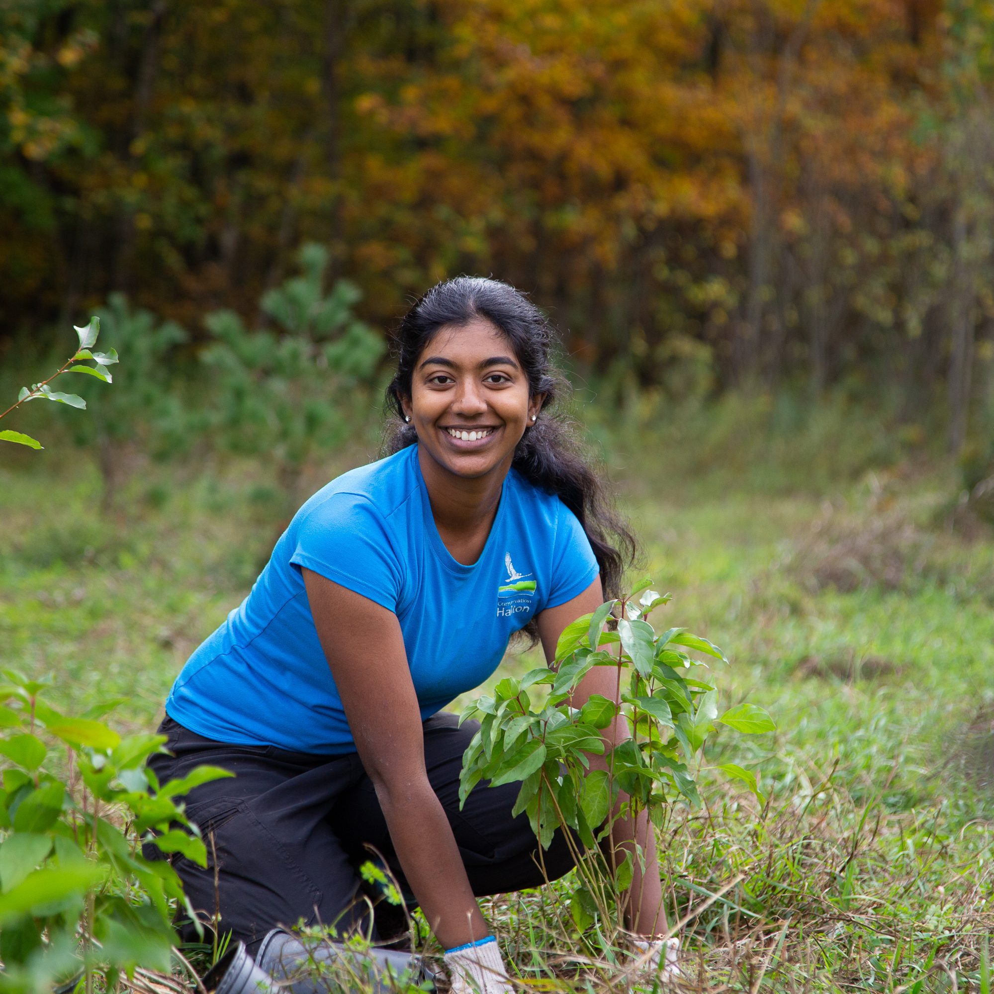Une femme sourit à l'appareil photo alors qu'elle plante un arbre.