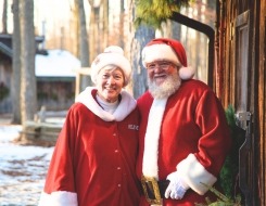 Santa and Mrs. Claus standing near a log cabin